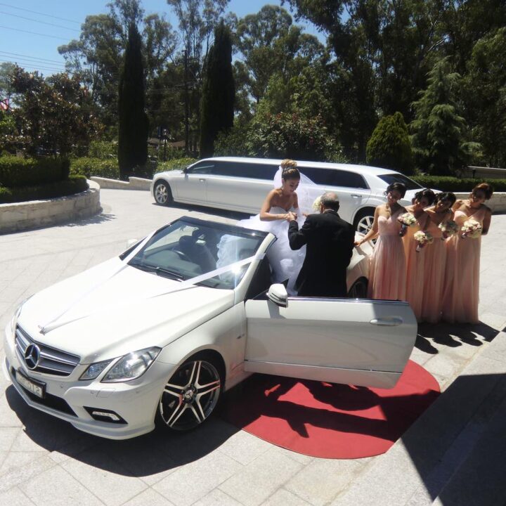 Chauffeur assisting bride out of convertible after arriving at wedding