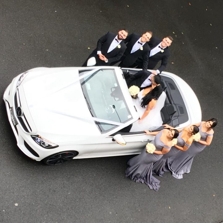View from above of newly weds kissing in our Mercedes convertible as the bridesmaids and groomsmen stand either side of the vehicle.
