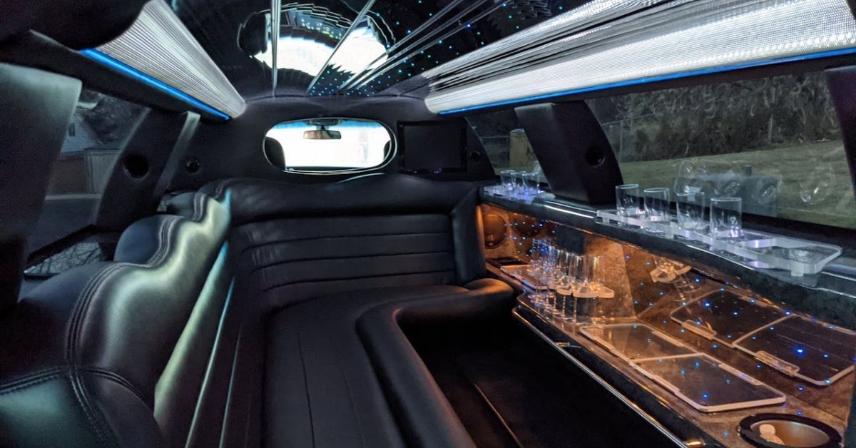 Luxurious black leather interior of a limousine featuring ambient lighting, a mirrored ceiling, and a fully stocked bar with glassware.