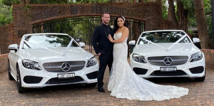 Bridge and groom posing with 2 convertible wedding cars.