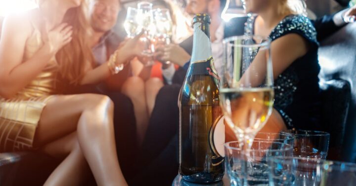 Women and men celebrating with drinks in a limousine car.