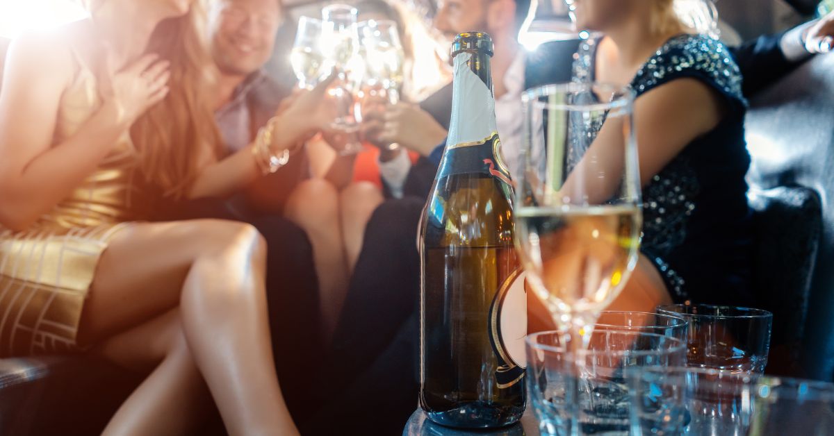 Women and men celebrating with drinks in a limousine car.