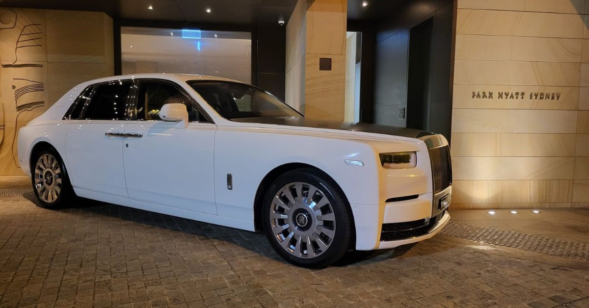A white Rolls-Royce luxury sedan parked outside the Park Hyatt Sydney entrance at night, illuminated by warm exterior lighting.