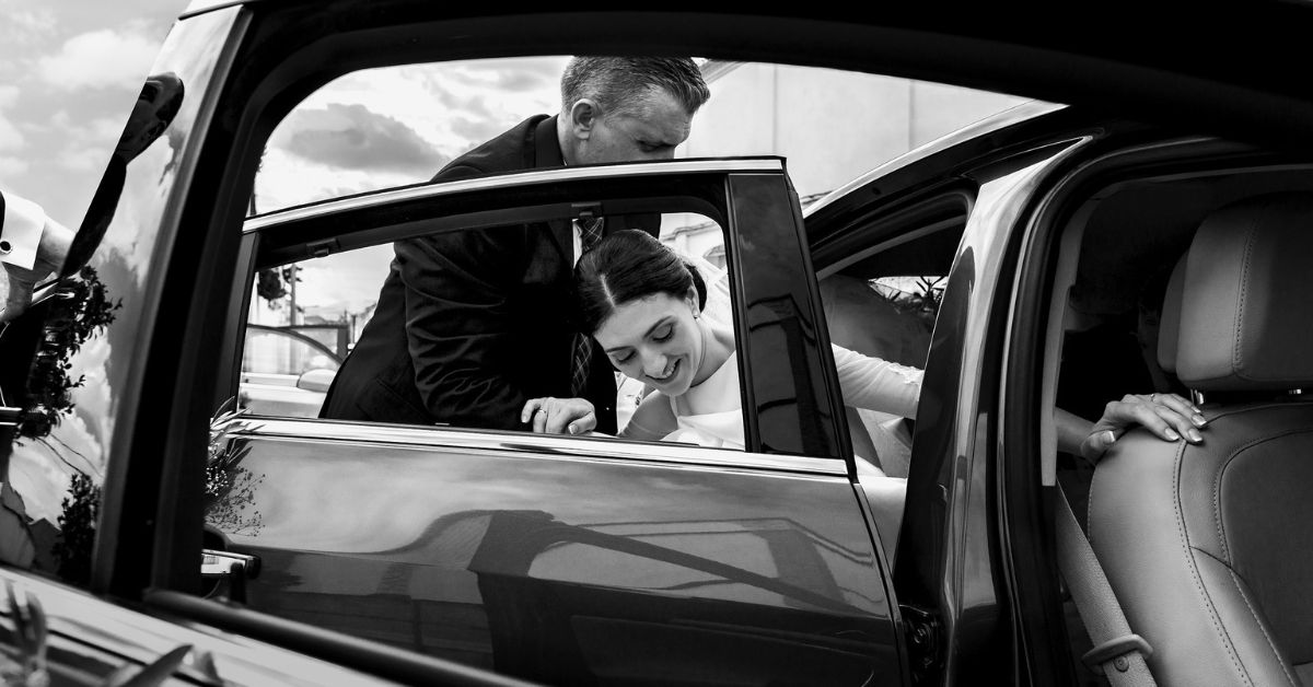 The groom assisting the bride on getting out of their wedding car.