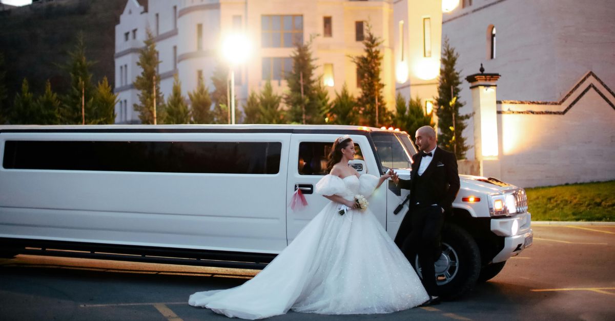 A bride and groom pose in front of a limo.