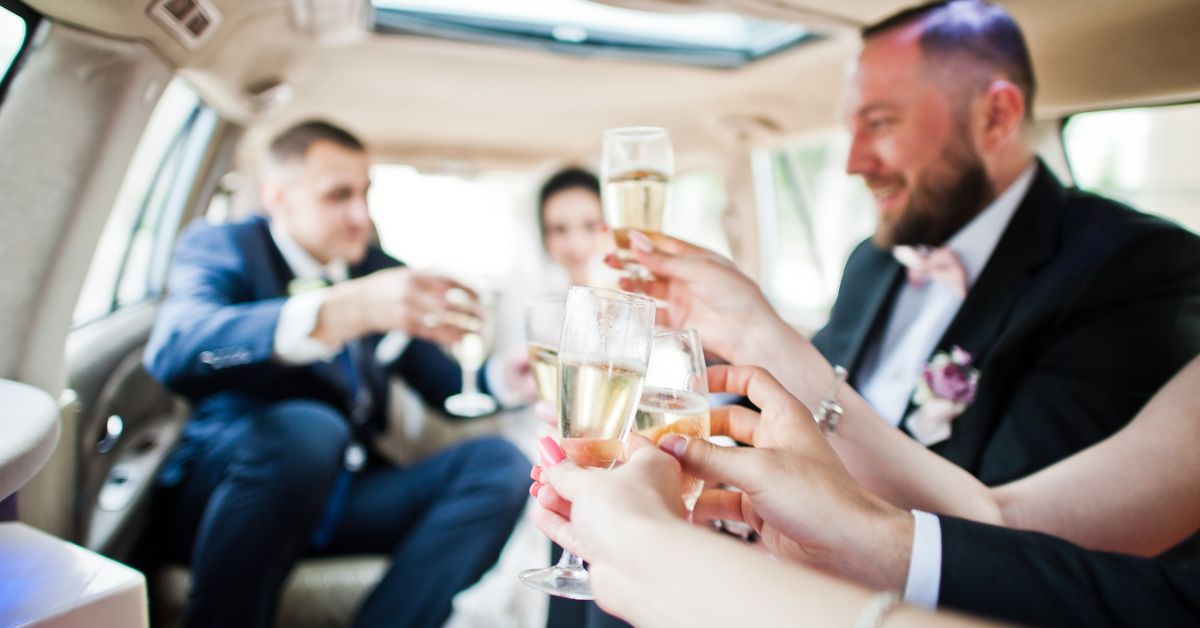 Wedding party celebrating inside a luxury limousine, raising champagne glasses for a toast while dressed in formal wedding attire.